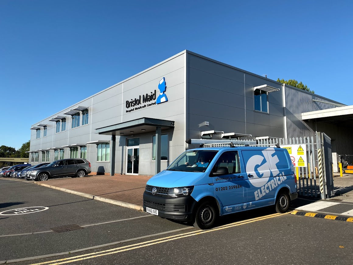 Modern industrial building with 'Bristol Maid' sign, parked cars, and a blue electrical service van