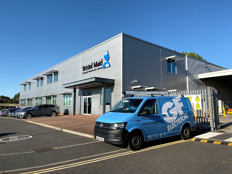 Modern industrial building with 'Bristol Maid' sign, parked cars, and a blue electrical service van