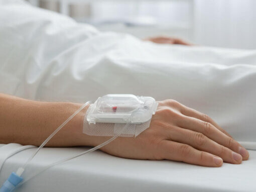 IV catheter secured with transparent medical glove on patient's hand in hospital bed
