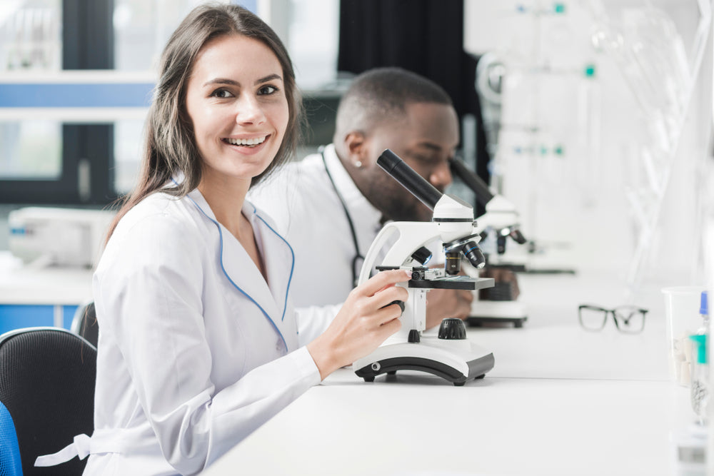 Female scientist in lab coat using microscope in bright laboratory setting