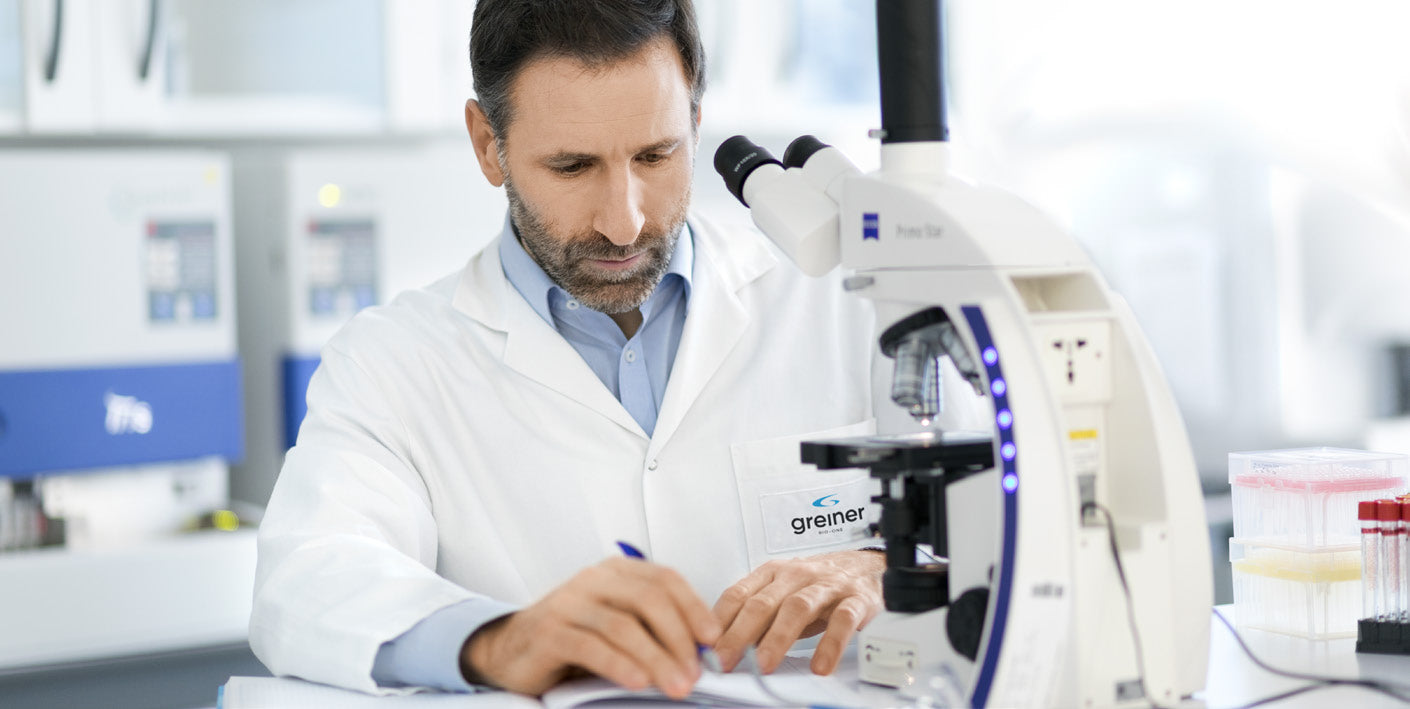 Scientist in lab coat using microscope in modern laboratory, medical research equipment visible