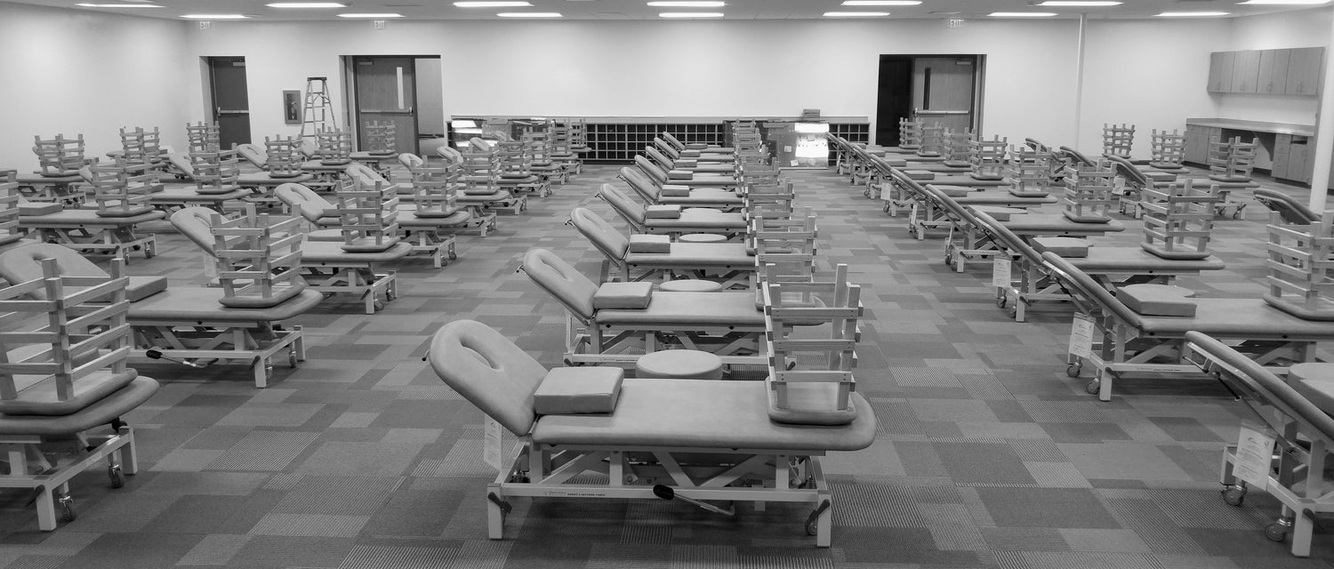 Medical supply room with rows of adjustable medical exam tables on wheels