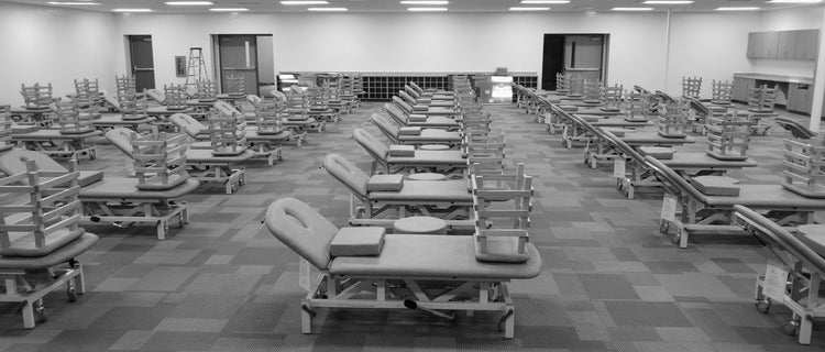 Medical supply room with rows of adjustable medical exam tables on wheels