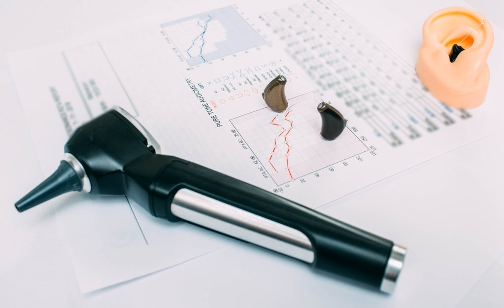 Otoscope, hearing aids, and ear model on audiometry test chart for hearing assessment