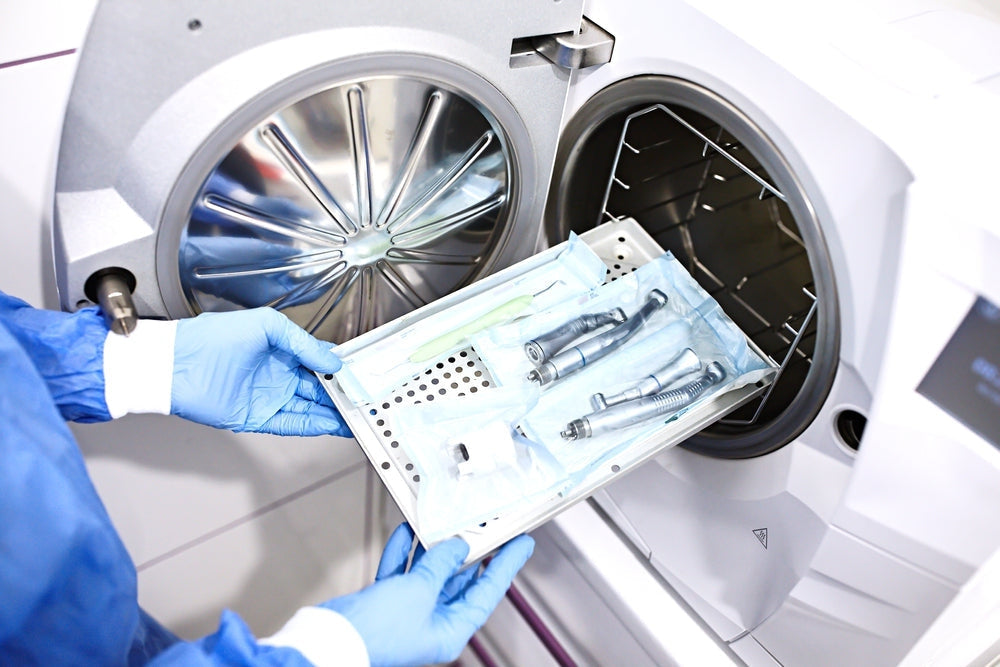 Gloved hands loading dental instruments into a medical autoclave sterilizer
