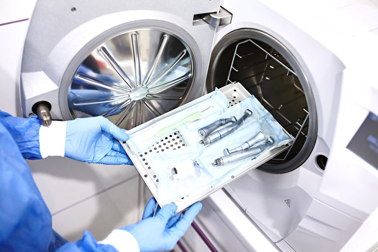 Gloved hands loading dental instruments into a medical autoclave sterilizer