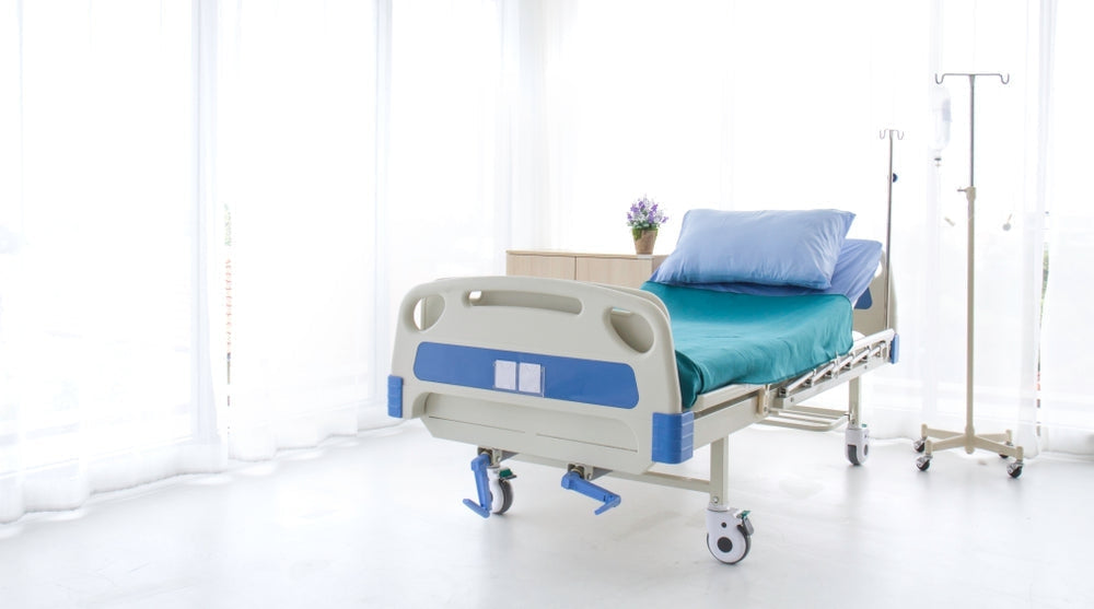 Hospital bed with teal bedding, IV stand, and medical furniture in a bright room
