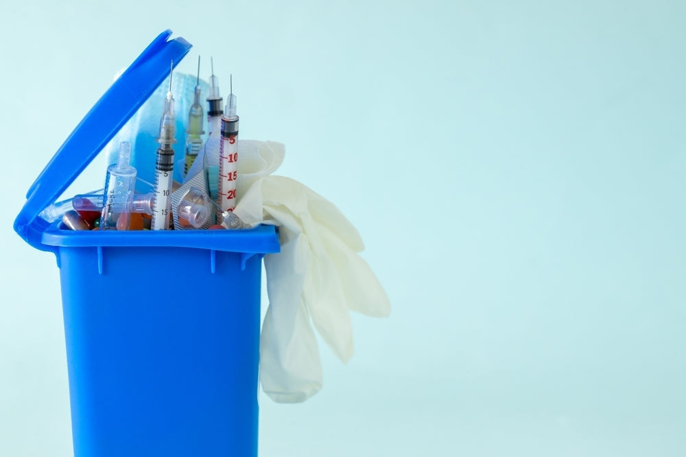 Medical sharps bin with used syringes and gloves for clinical waste disposal