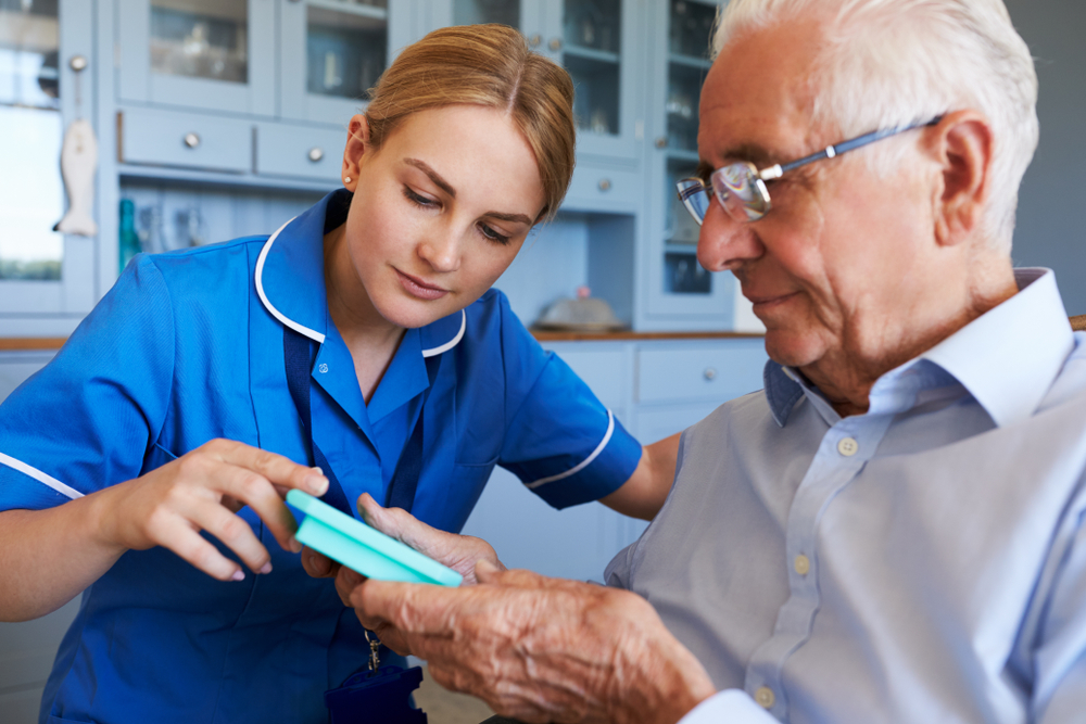 Nurse assisting elderly man with medication in pill organizer at home