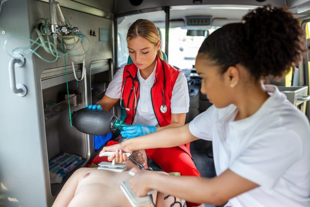 Paramedics using defibrillator and resuscitation bag on patient in ambulance