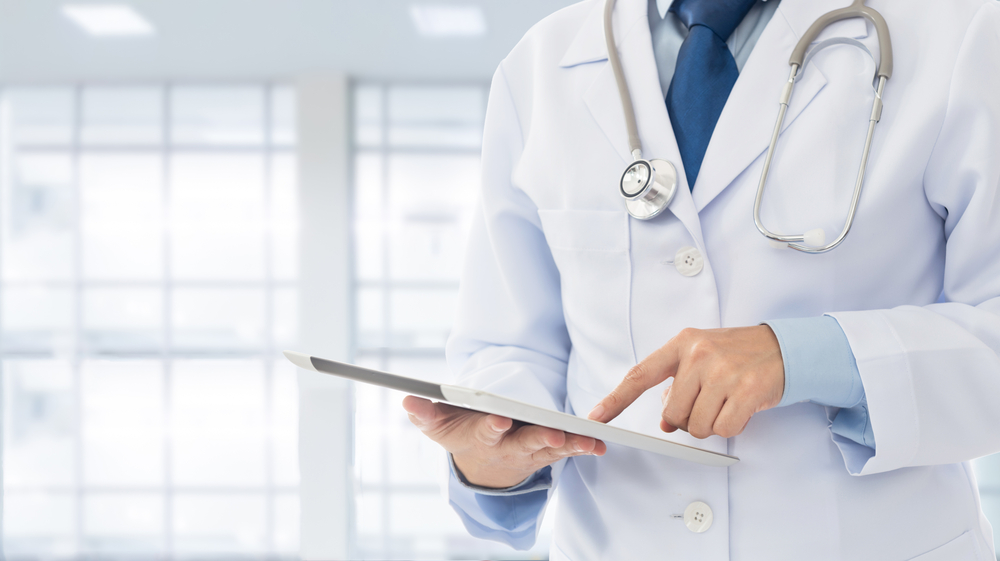 Doctor in medical uniform with stethoscope using digital tablet in hospital office