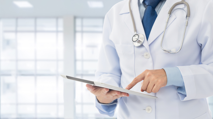 Doctor in medical uniform with stethoscope using digital tablet in hospital office