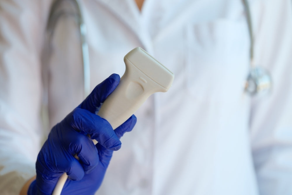 Medical professional with blue gloves holding ultrasound Doppler probe