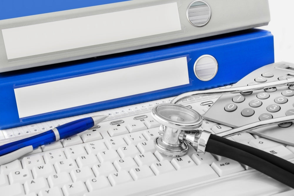 Medical office desk with stethoscope, blue and gray folders, keyboard, pen, and calculator