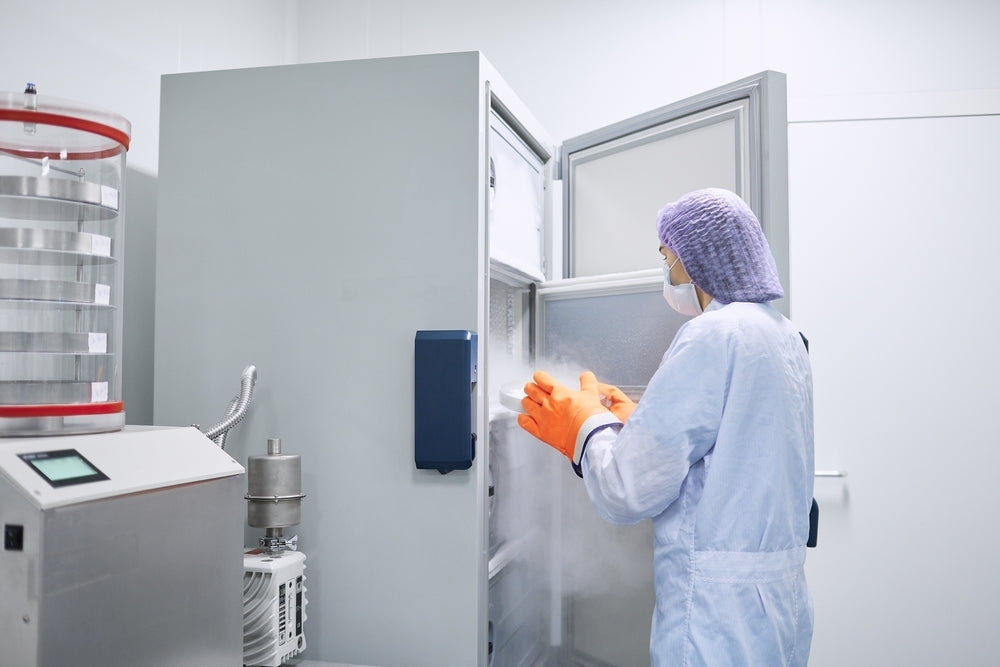 Lab technician in PPE using medical freezer in sterile laboratory environment