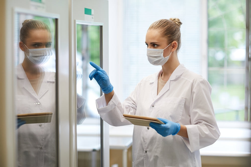 Female lab technician in medical mask and gloves using laboratory fridge in clinical setting