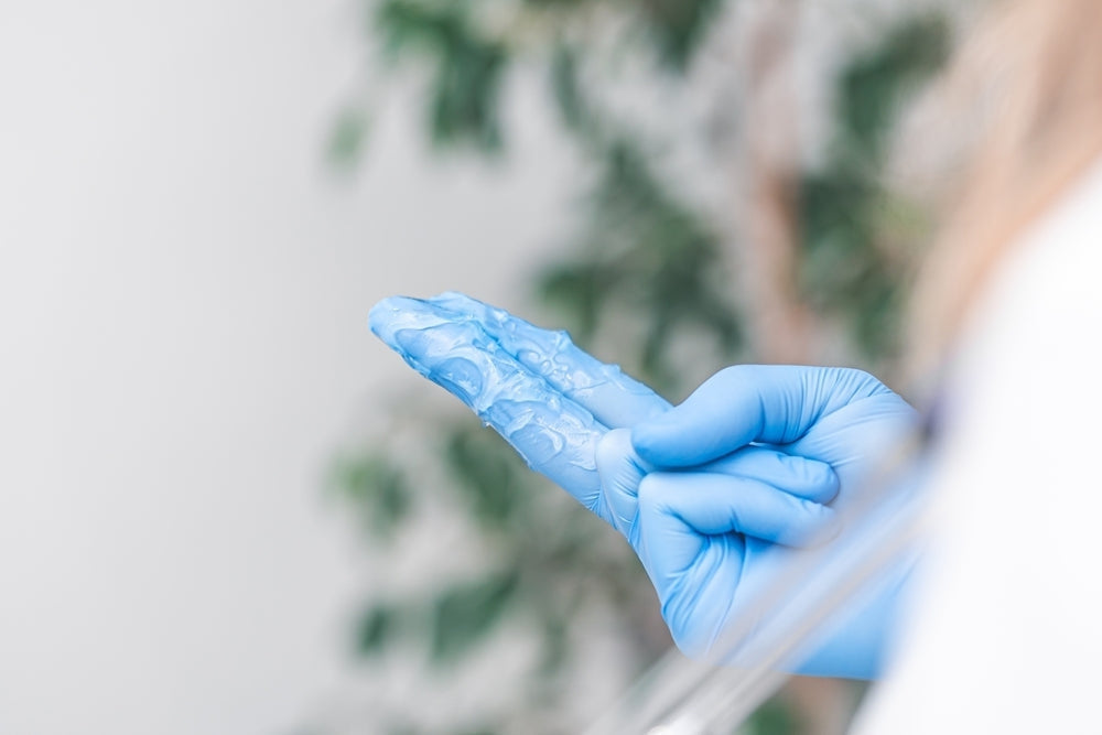 Blue gloved hand with clear medical gel, clinical setting, medical supplies concept