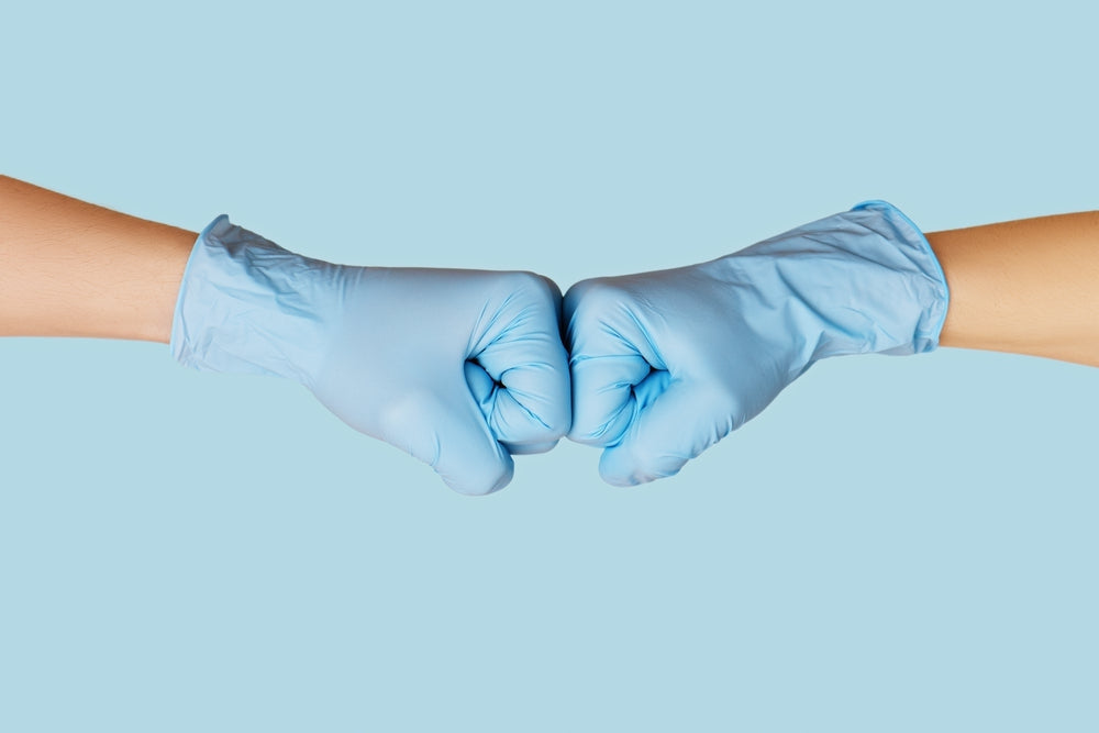 Two hands wearing blue disposable medical gloves performing a fist bump on blue background