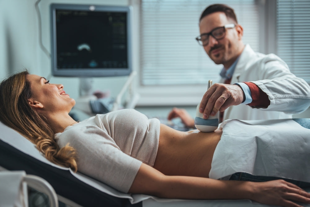 Doctor performing abdominal ultrasound scan on smiling woman in clinic
