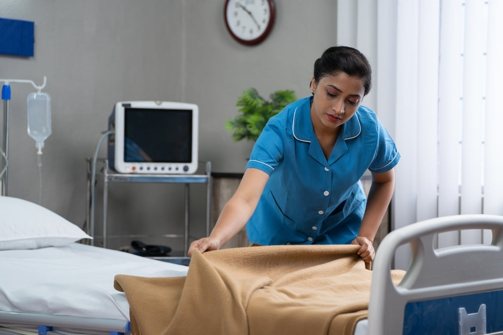 Nurse making hospital bed in medical facility with monitoring equipment and IV stand