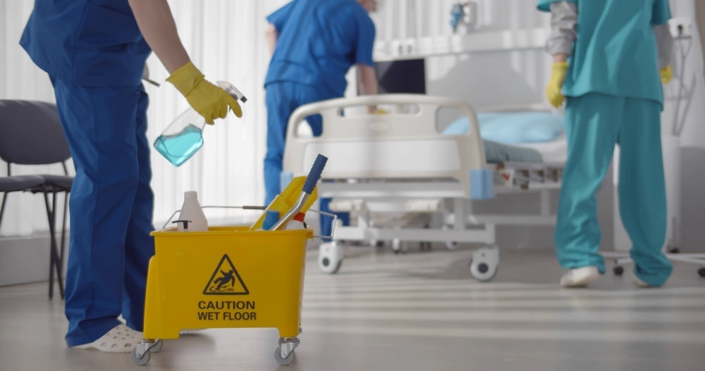 Hospital cleaning staff with yellow caution wet floor sign and cleaning equipment by patient bed