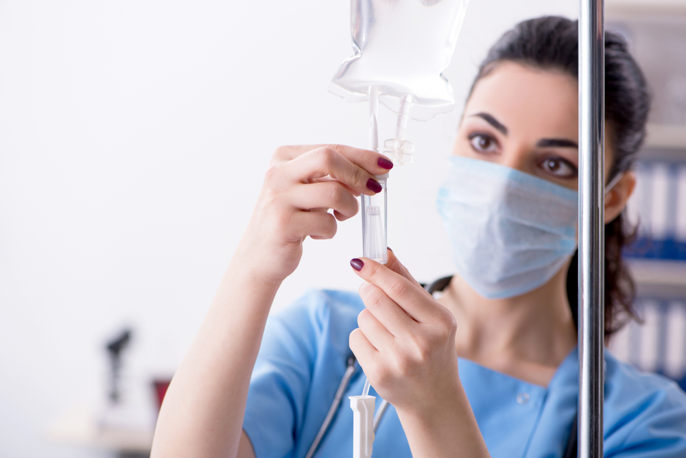 Nurse with mask preparing IV infusion drip in medical setting