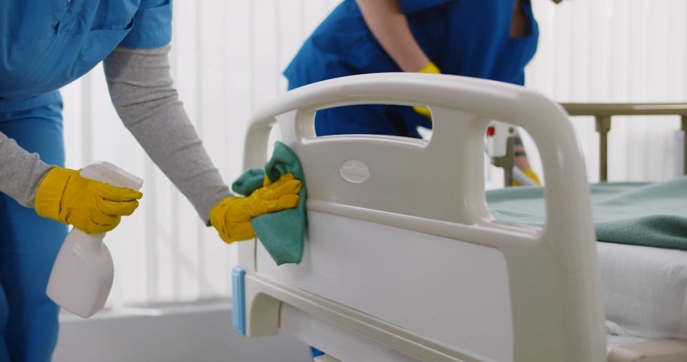 Janitorial staff cleaning hospital bed with disinfectant spray and gloves