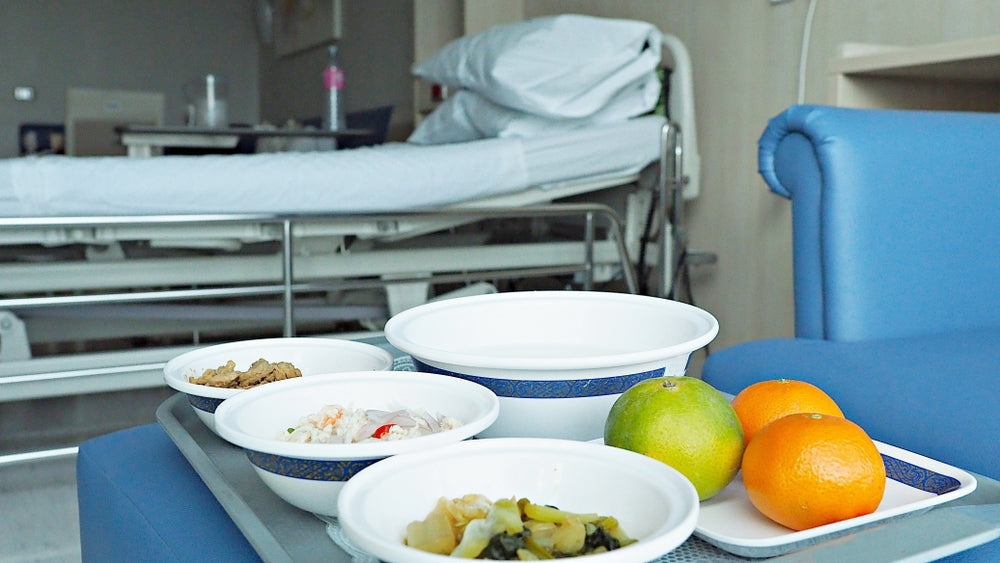 Hospital bed and medical food trays with healthy meals and fruits in a patient room