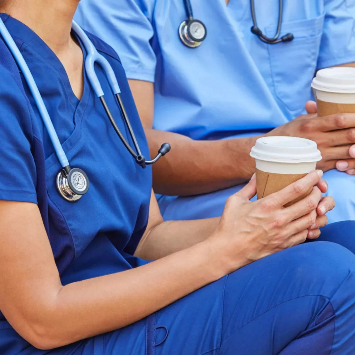 Healthcare professionals in scrubs with stethoscopes, holding takeaway coffee cups.
