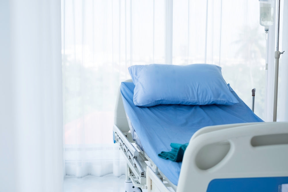 Hospital bed with blue mattress, pillow, and blanket in a bright patient room