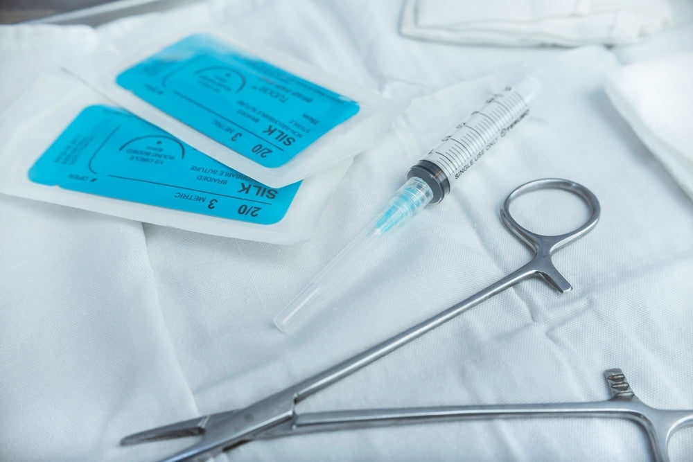 Sterile surgical instruments, syringe, and suture packs on a white medical drape