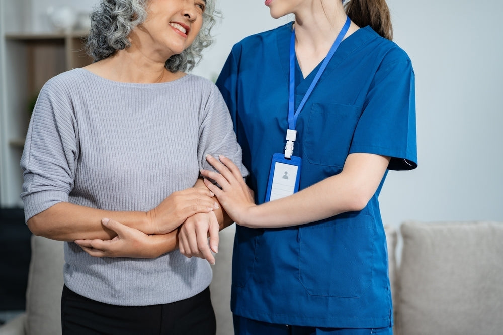 Nurse in blue scrubs assisting smiling elderly woman at home, nursing equipment care