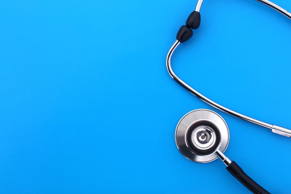 Classic stethoscope with black tubing on blue background, medical equipment product photo