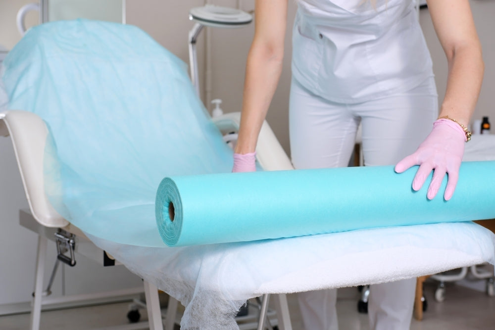 Medical professional covering examination table with blue disposable paper roll in clinic