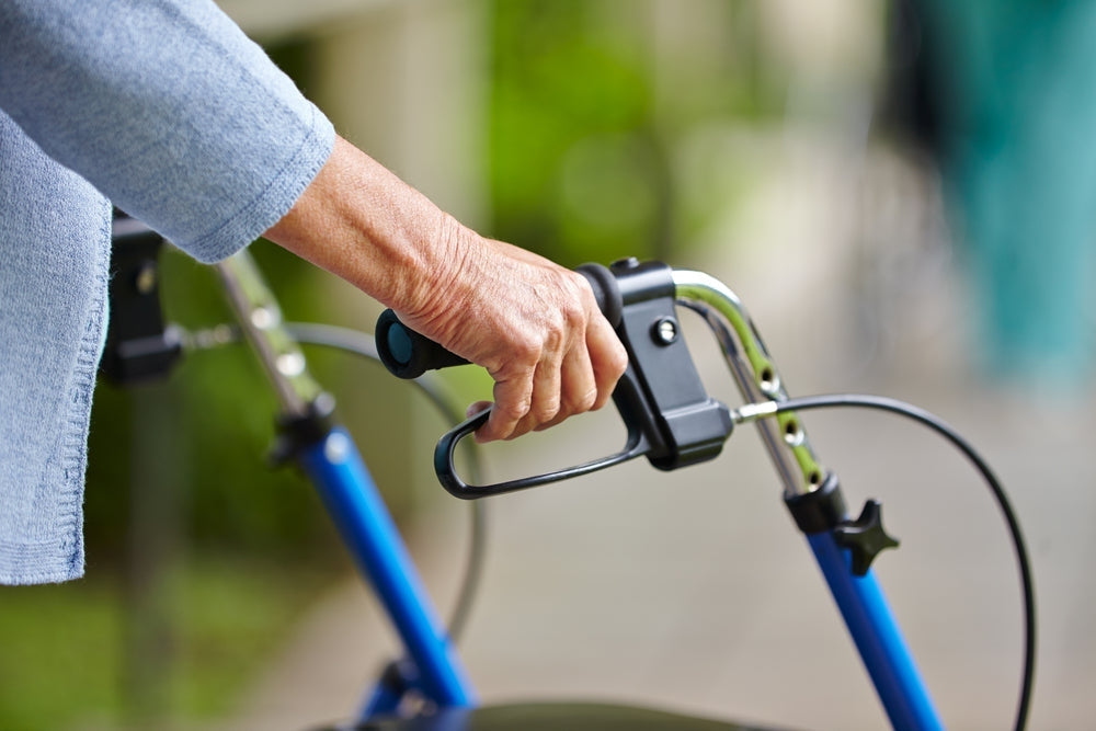 Senior using blue mobility walker outdoors, focus on hand and handle for patient handling aid