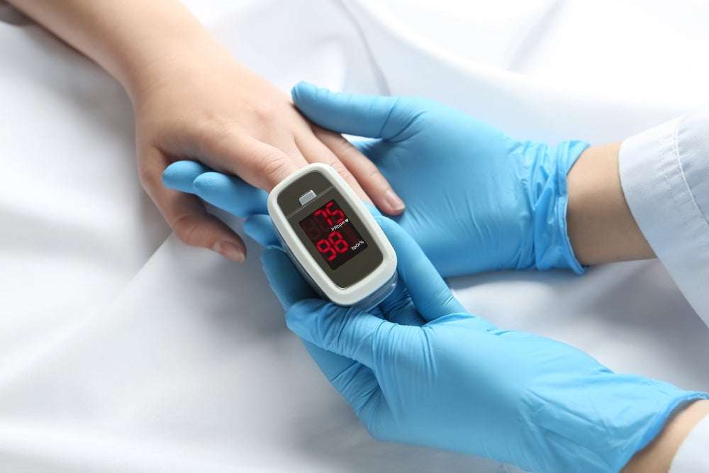 Gloved hands using a pulse oximeter to check blood oxygen on a patient's finger