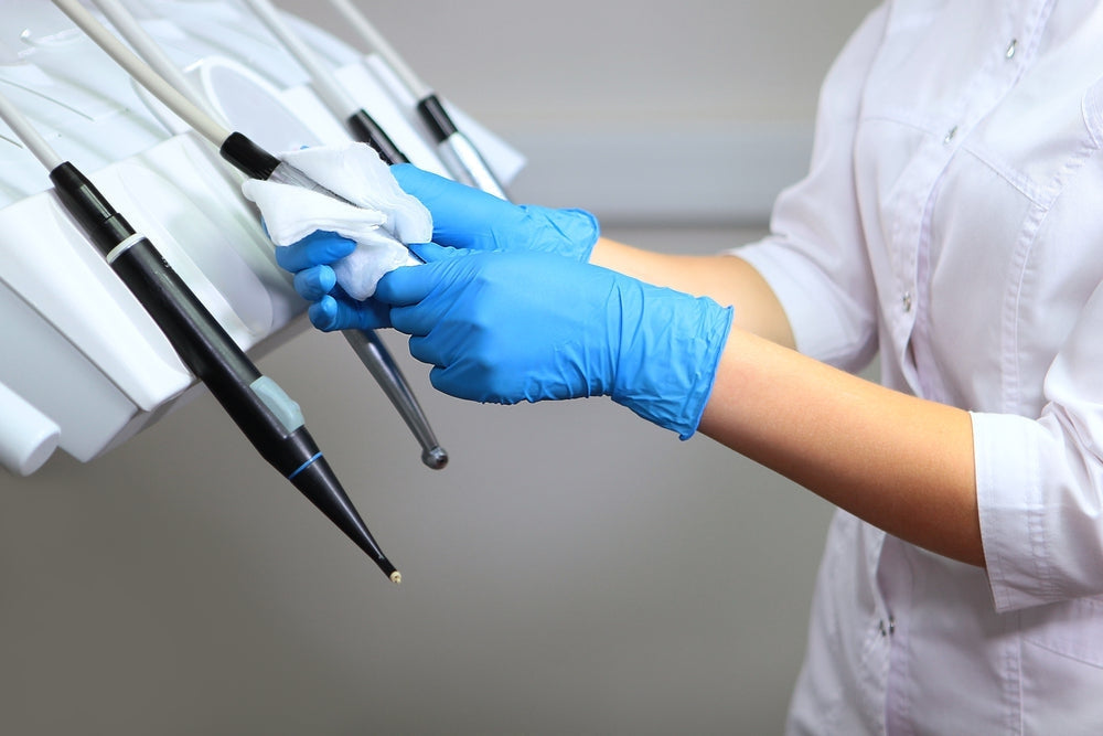 Gloved hands using sanitising wipes to clean dental equipment in a medical setting