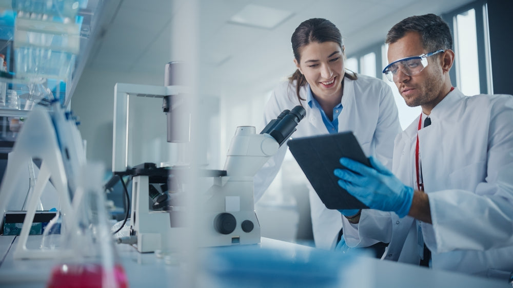Scientists in lab coats reviewing data on tablet near microscope in medical laboratory