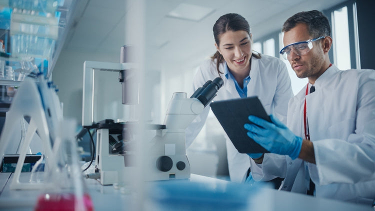 Scientists in lab coats reviewing data on tablet near microscope in medical laboratory