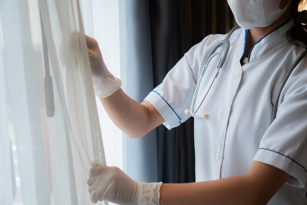 Nurse in medical uniform and mask opening curtains in a healthcare setting