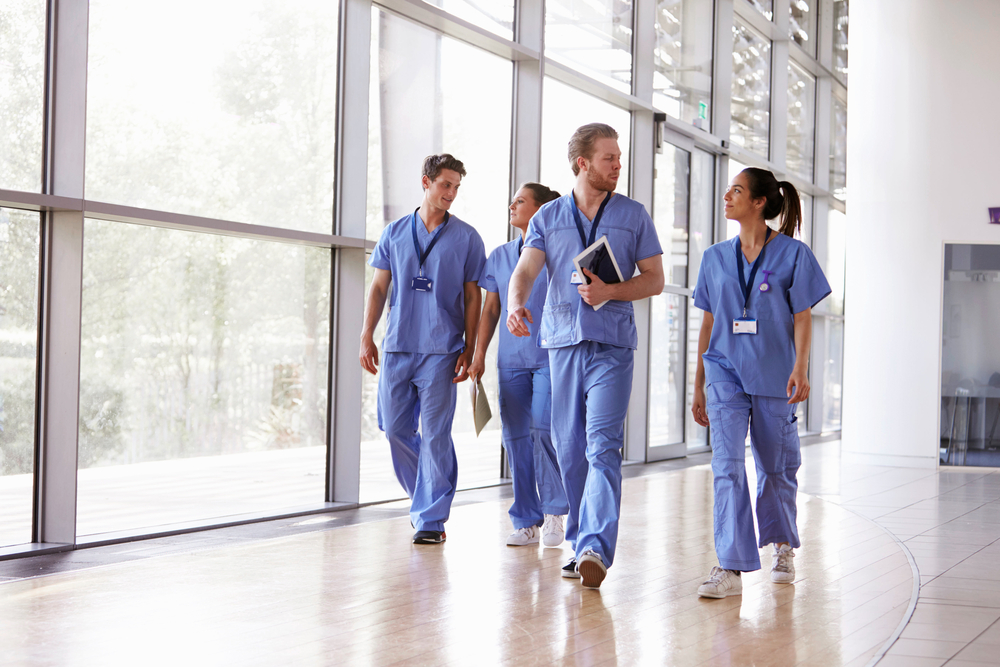 Healthcare professionals in blue medical scrubs walking in a bright hospital corridor