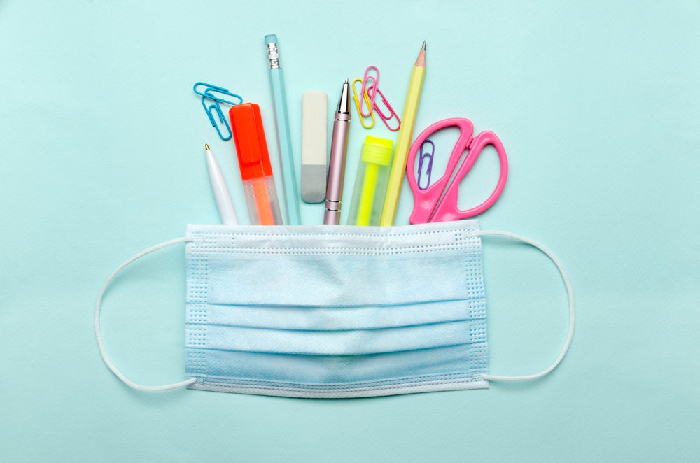 Assorted stationery items and a medical face mask on a light blue background