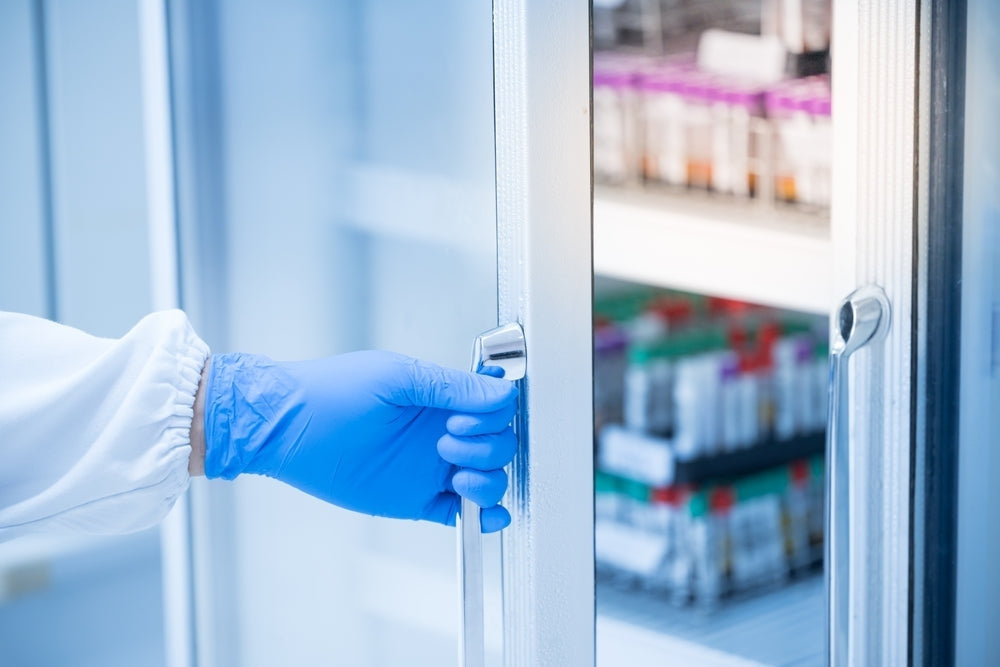 Gloved hand opening medical refrigerator with laboratory sample storage inside