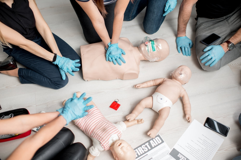 Group practicing CPR on adult, child, and infant medical training dummies with gloves
