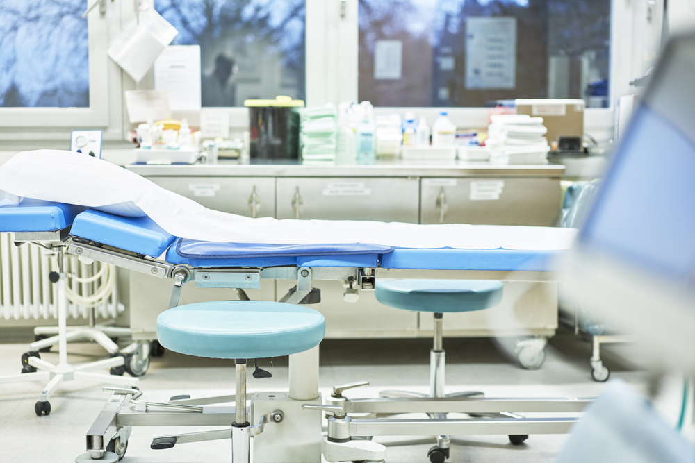 Modern treatment room with blue medical examination chair and adjustable stools