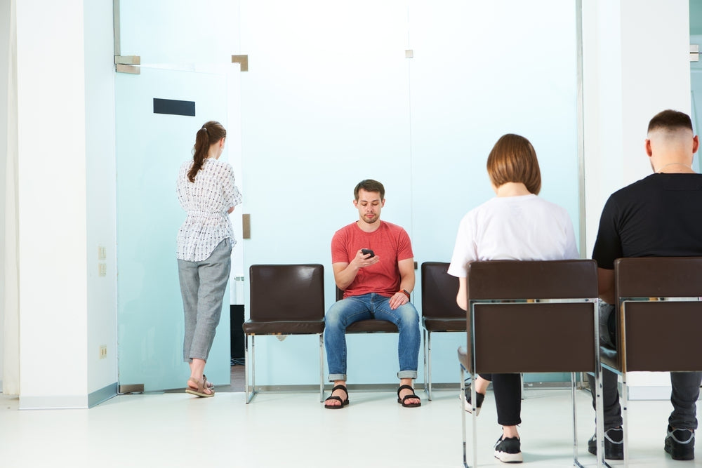 People sitting in a bright medical waiting room with modern chairs and glass doors.