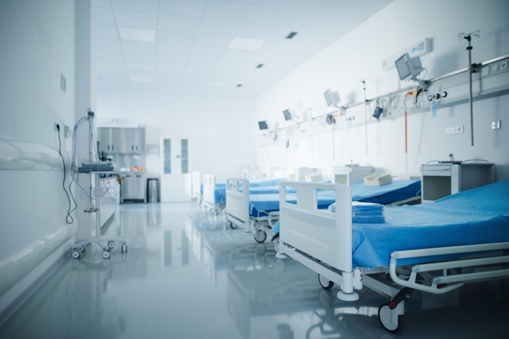 Row of empty hospital beds with blue sheets and medical equipment in a modern ward