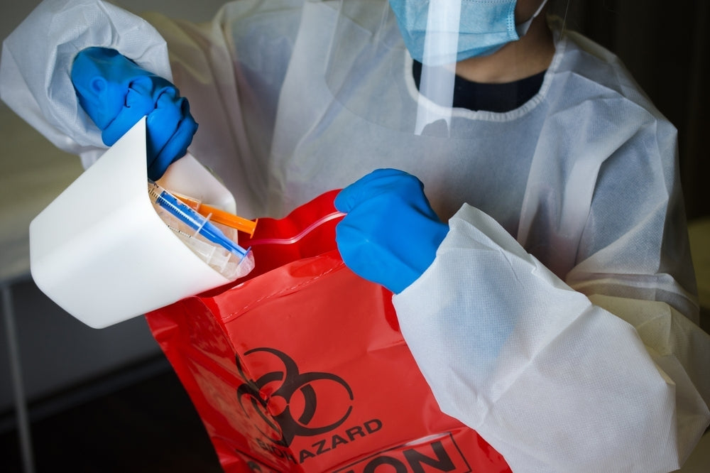 Healthcare worker in PPE disposing clinical waste into red biohazard bag